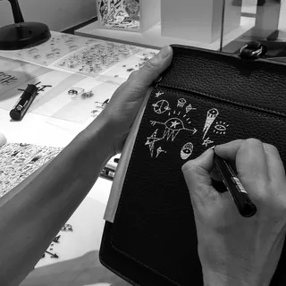 Hands creating white abstract doodles on black leather with marker