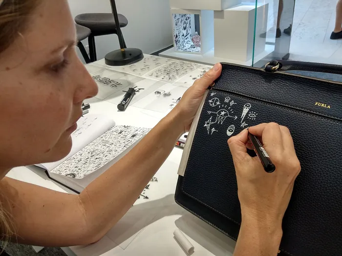 Hand drawing white doodles on black leather purse with pen