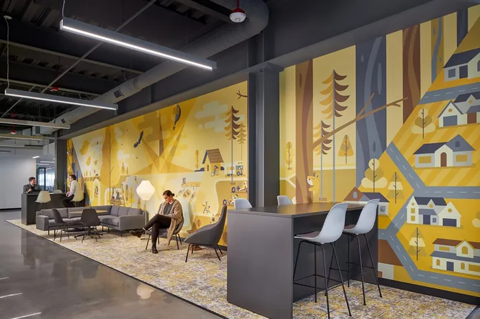 Office lounge with yellow mural, gray chairs, and bar stools